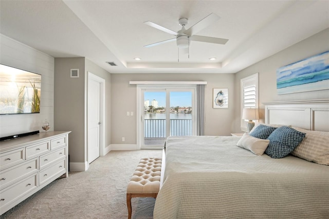 carpeted bedroom featuring a water view, ceiling fan, a raised ceiling, and access to outside