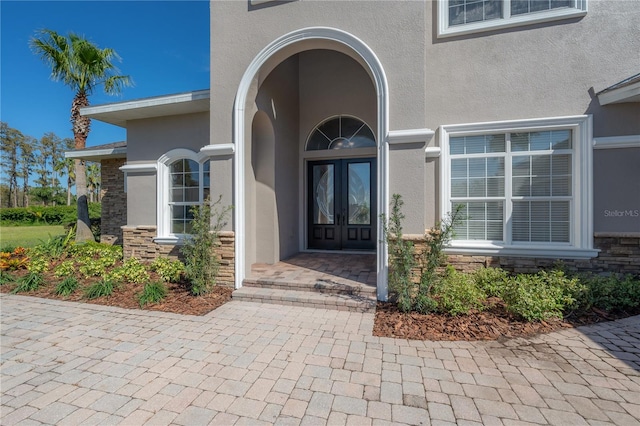 view of exterior entry with stone siding, stucco siding, and french doors