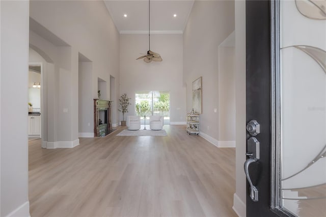 entryway with ceiling fan, a towering ceiling, light hardwood / wood-style flooring, and ornamental molding