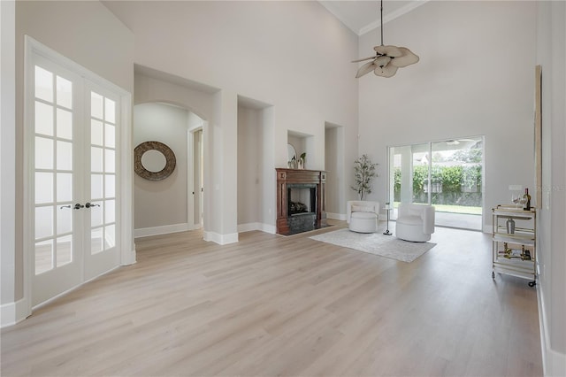 unfurnished living room with french doors, ceiling fan, a towering ceiling, and light hardwood / wood-style flooring