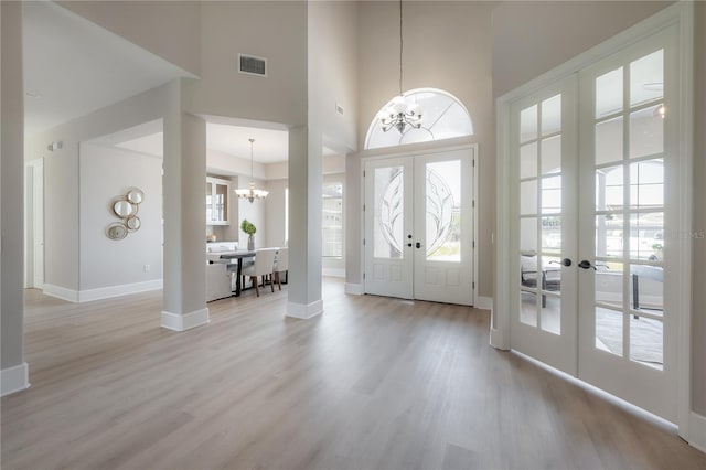 foyer with light hardwood / wood-style flooring, french doors, a chandelier, and a high ceiling