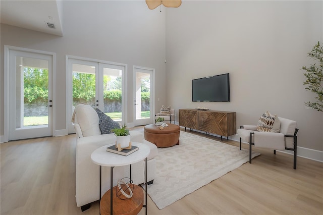 living room with a towering ceiling, french doors, light hardwood / wood-style flooring, and a healthy amount of sunlight