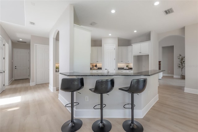 kitchen featuring white cabinetry, light hardwood / wood-style floors, and dark stone counters