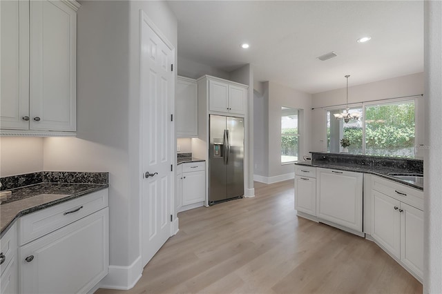 kitchen with stainless steel fridge, white cabinetry, light hardwood / wood-style floors, dark stone countertops, and a chandelier