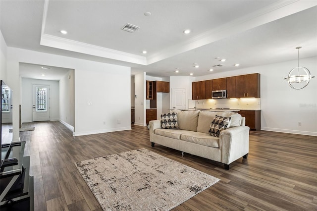 living room with a tray ceiling, ornamental molding, dark hardwood / wood-style flooring, and a chandelier