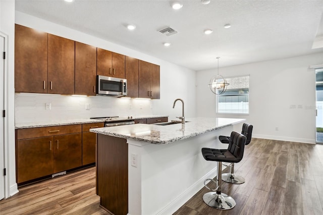 kitchen with an island with sink, hanging light fixtures, wood-type flooring, sink, and a breakfast bar