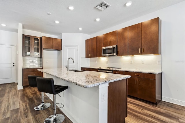 kitchen featuring a center island with sink, tasteful backsplash, sink, stainless steel appliances, and dark hardwood / wood-style floors