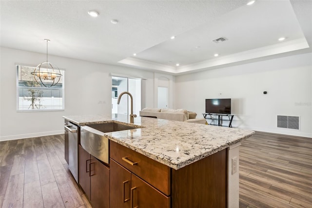 kitchen with a tray ceiling, dark hardwood / wood-style flooring, and an island with sink