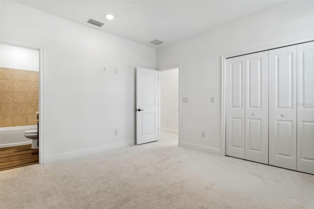 unfurnished bedroom with light carpet, ensuite bathroom, and a closet