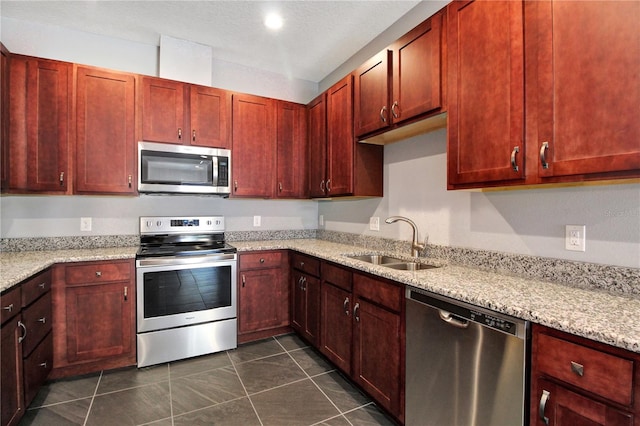 kitchen with light stone counters, stainless steel appliances, sink, and dark tile patterned floors