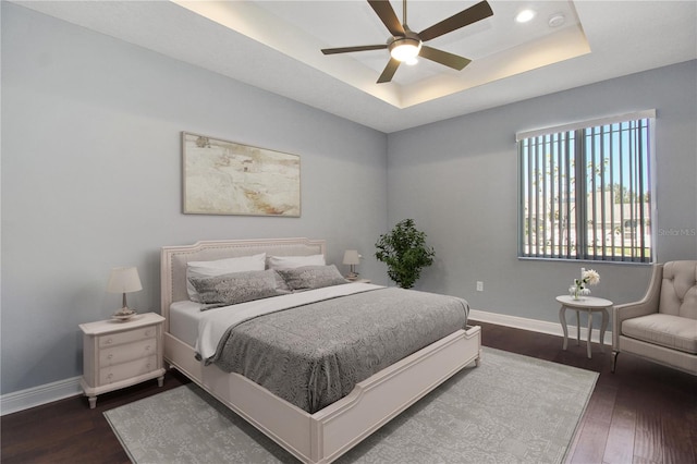 bedroom with dark hardwood / wood-style flooring, a tray ceiling, and ceiling fan