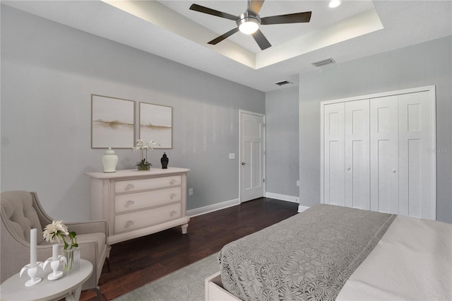 bedroom with a closet, dark hardwood / wood-style floors, a tray ceiling, and ceiling fan