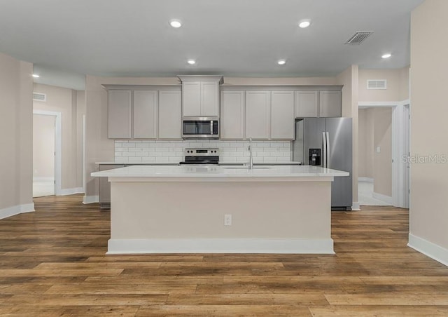 kitchen with stainless steel appliances, gray cabinets, sink, and a center island with sink