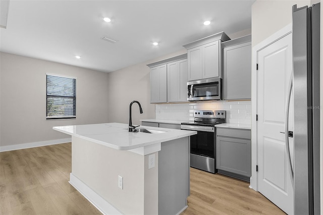 kitchen featuring sink, gray cabinetry, an island with sink, stainless steel appliances, and light hardwood / wood-style floors