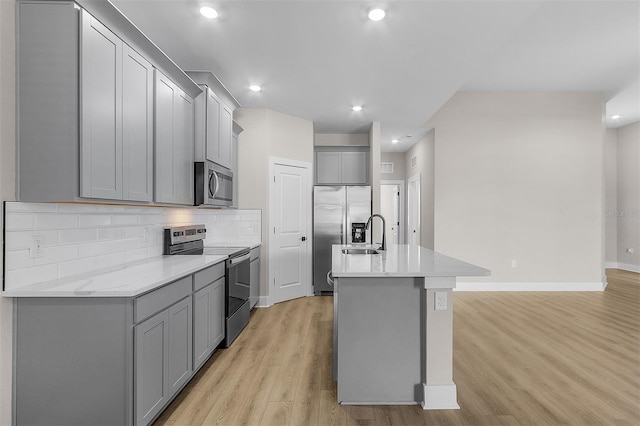 kitchen featuring gray cabinetry, light hardwood / wood-style flooring, an island with sink, stainless steel appliances, and backsplash