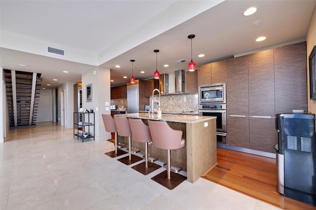 kitchen with light stone counters, a kitchen island with sink, a kitchen bar, stainless steel appliances, and decorative light fixtures