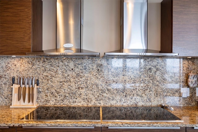 interior details featuring wall chimney range hood, decorative backsplash, exhaust hood, stone countertops, and black electric stovetop