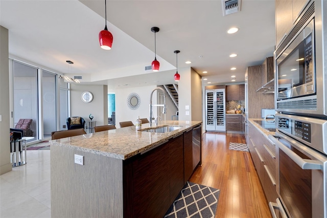 kitchen featuring a center island with sink, appliances with stainless steel finishes, light stone countertops, light hardwood / wood-style flooring, and pendant lighting