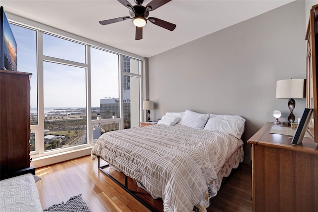 bedroom with multiple windows, a wall of windows, wood-type flooring, and ceiling fan