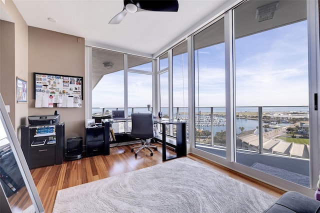 office with a wall of windows, hardwood / wood-style floors, a water view, and ceiling fan