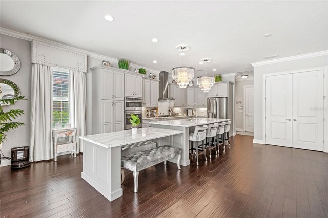 kitchen featuring wall chimney range hood, a large island with sink, appliances with stainless steel finishes, and ornamental molding