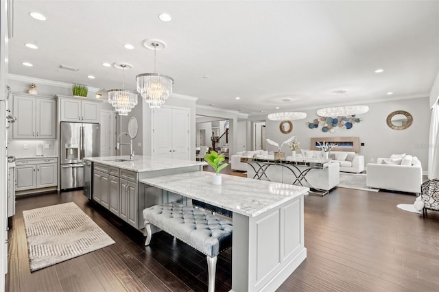 kitchen with a large island with sink, dark hardwood / wood-style flooring, light stone counters, a breakfast bar area, and stainless steel refrigerator with ice dispenser