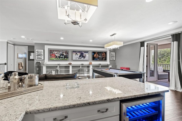 kitchen with crown molding, dark hardwood / wood-style flooring, hanging light fixtures, beverage cooler, and light stone counters