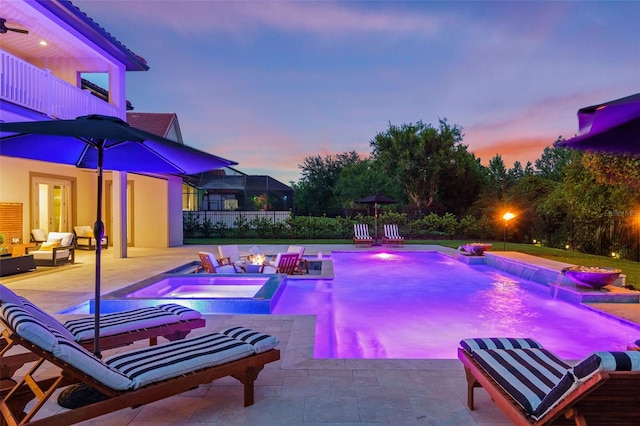 pool at dusk with a patio area, pool water feature, an in ground hot tub, and glass enclosure