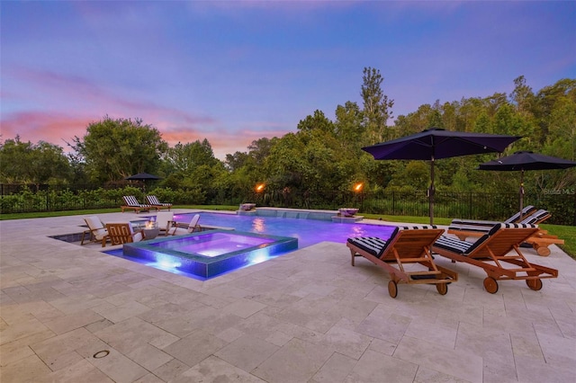 pool at dusk with an in ground hot tub, pool water feature, and a patio area