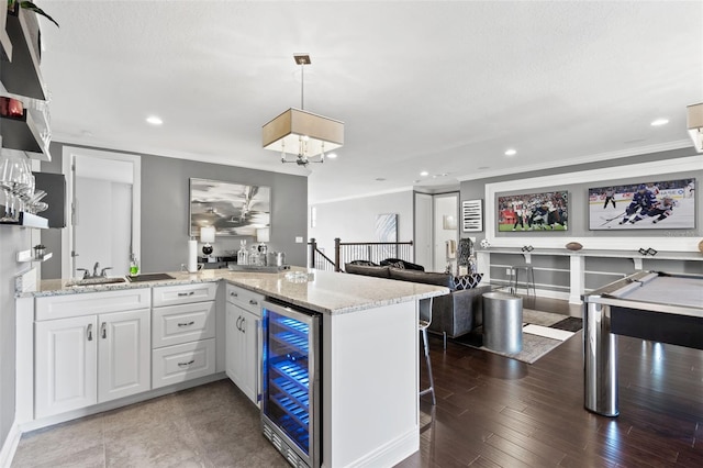 kitchen featuring white cabinets, beverage cooler, hardwood / wood-style flooring, pendant lighting, and light stone counters