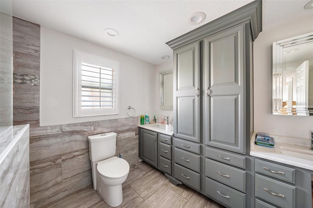 bathroom featuring vanity, a textured ceiling, toilet, and tile walls