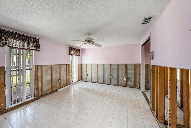 unfurnished room featuring ceiling fan, a textured ceiling, and tile walls