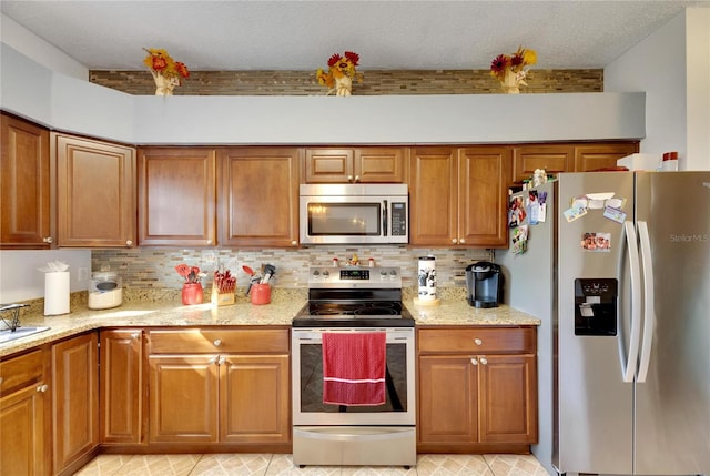 kitchen with decorative backsplash, appliances with stainless steel finishes, light stone counters, and a textured ceiling