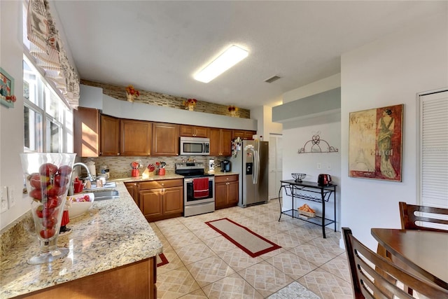 kitchen with appliances with stainless steel finishes, light tile patterned flooring, sink, backsplash, and light stone counters