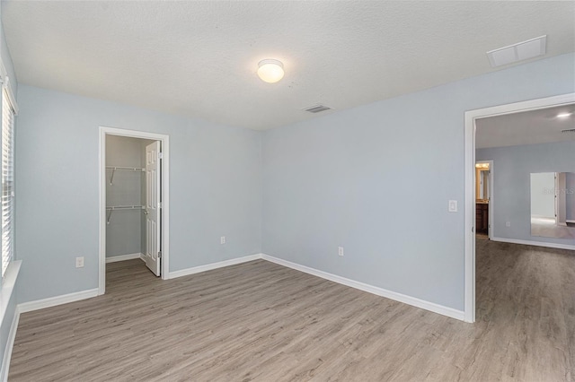 unfurnished bedroom featuring a closet, light hardwood / wood-style floors, a textured ceiling, and a walk in closet