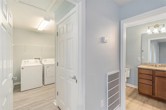 clothes washing area featuring a textured ceiling, sink, washer and clothes dryer, and light wood-type flooring