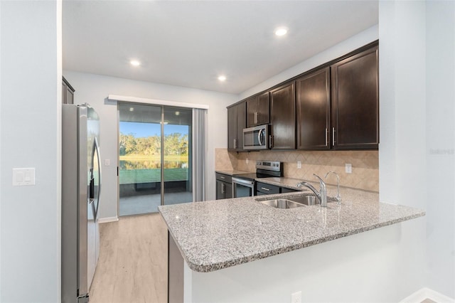 kitchen with light stone countertops, appliances with stainless steel finishes, sink, and kitchen peninsula