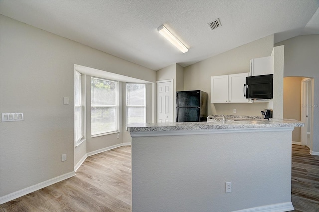 kitchen with white cabinetry, kitchen peninsula, vaulted ceiling, black appliances, and light wood-type flooring