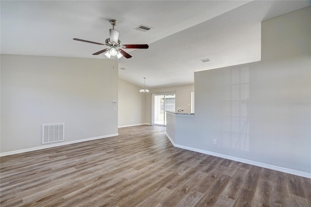 empty room featuring ceiling fan with notable chandelier, light hardwood / wood-style flooring, and lofted ceiling