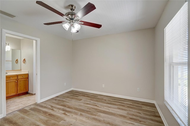 unfurnished bedroom with multiple windows, ensuite bathroom, ceiling fan, and light wood-type flooring