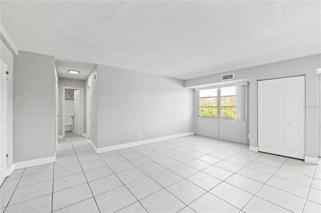 unfurnished bedroom with a textured ceiling, baseboards, light tile patterned floors, and visible vents