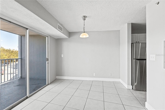 unfurnished room with a textured ceiling, baseboards, light tile patterned floors, and visible vents