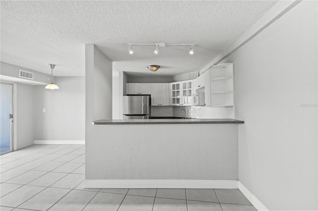 kitchen with glass insert cabinets, freestanding refrigerator, dark countertops, visible vents, and baseboards