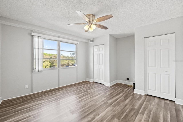 unfurnished bedroom with a textured ceiling, dark wood-type flooring, and ceiling fan