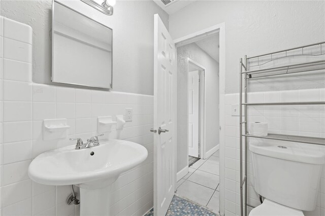 bathroom with tile walls, toilet, tile patterned flooring, and a wainscoted wall