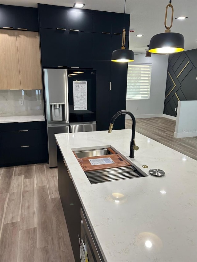 kitchen featuring light hardwood / wood-style floors, light stone counters, sink, stainless steel fridge with ice dispenser, and decorative light fixtures