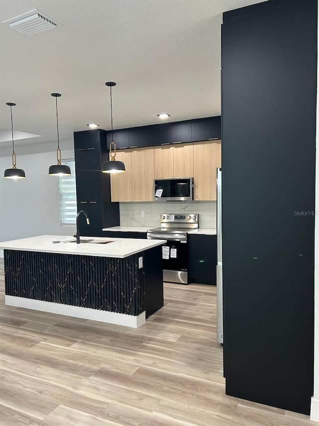 kitchen with an island with sink, light brown cabinetry, decorative light fixtures, and appliances with stainless steel finishes