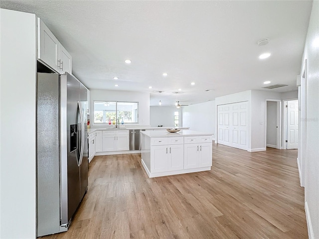 kitchen with light hardwood / wood-style floors, appliances with stainless steel finishes, a kitchen island, and white cabinets