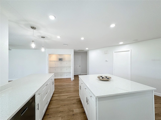 kitchen with white cabinets, hanging light fixtures, a kitchen island, light stone countertops, and dark wood-type flooring