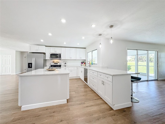 kitchen with white cabinets, hanging light fixtures, a kitchen island, appliances with stainless steel finishes, and light wood-type flooring